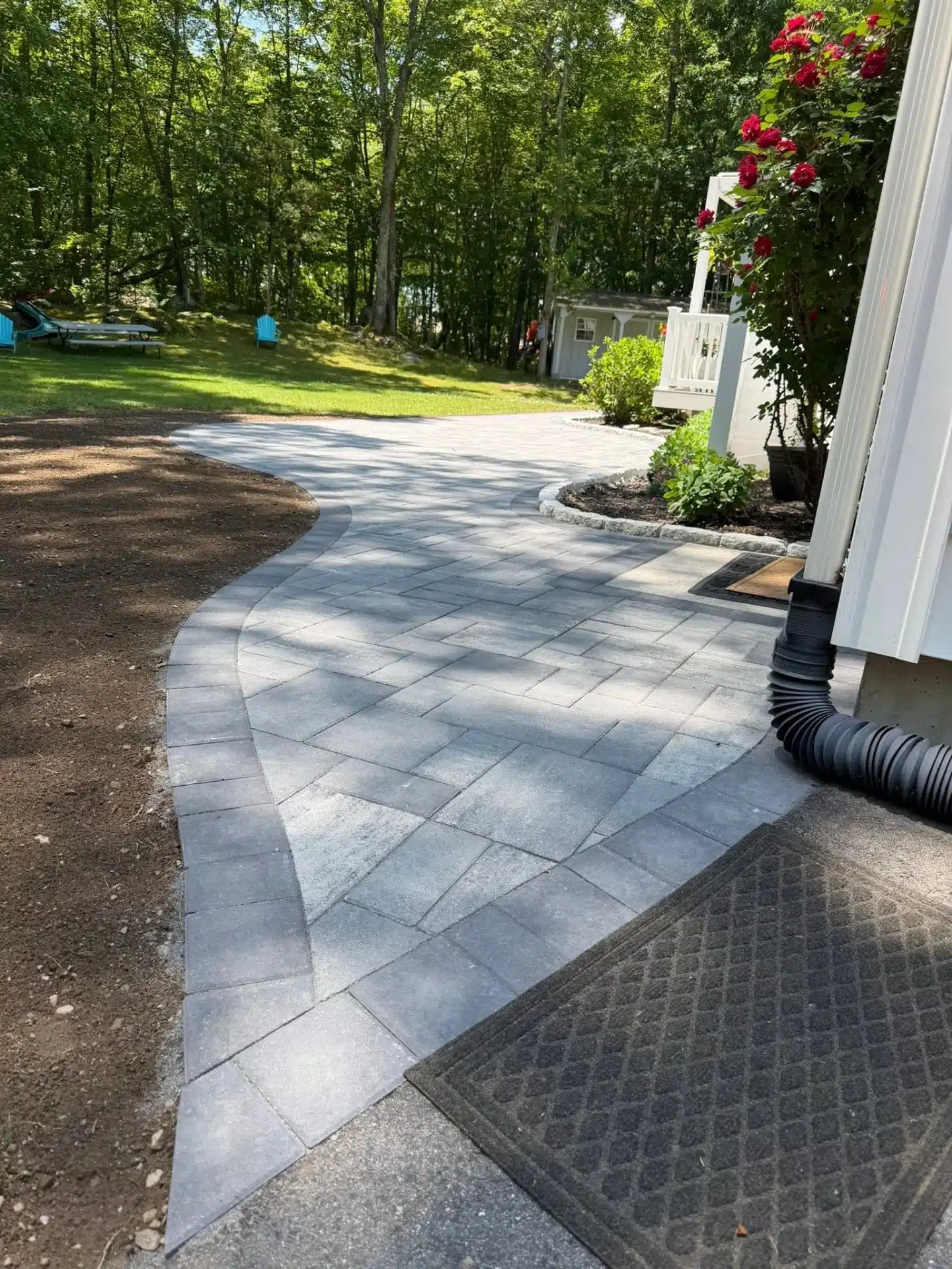 hardscaping-services-waterford-ct-spicers-lawn-care (2) Paver patio installation in Waterford, CT, featuring gray interlocking pavers, stone landscape borders, and access to backyard deck steps.