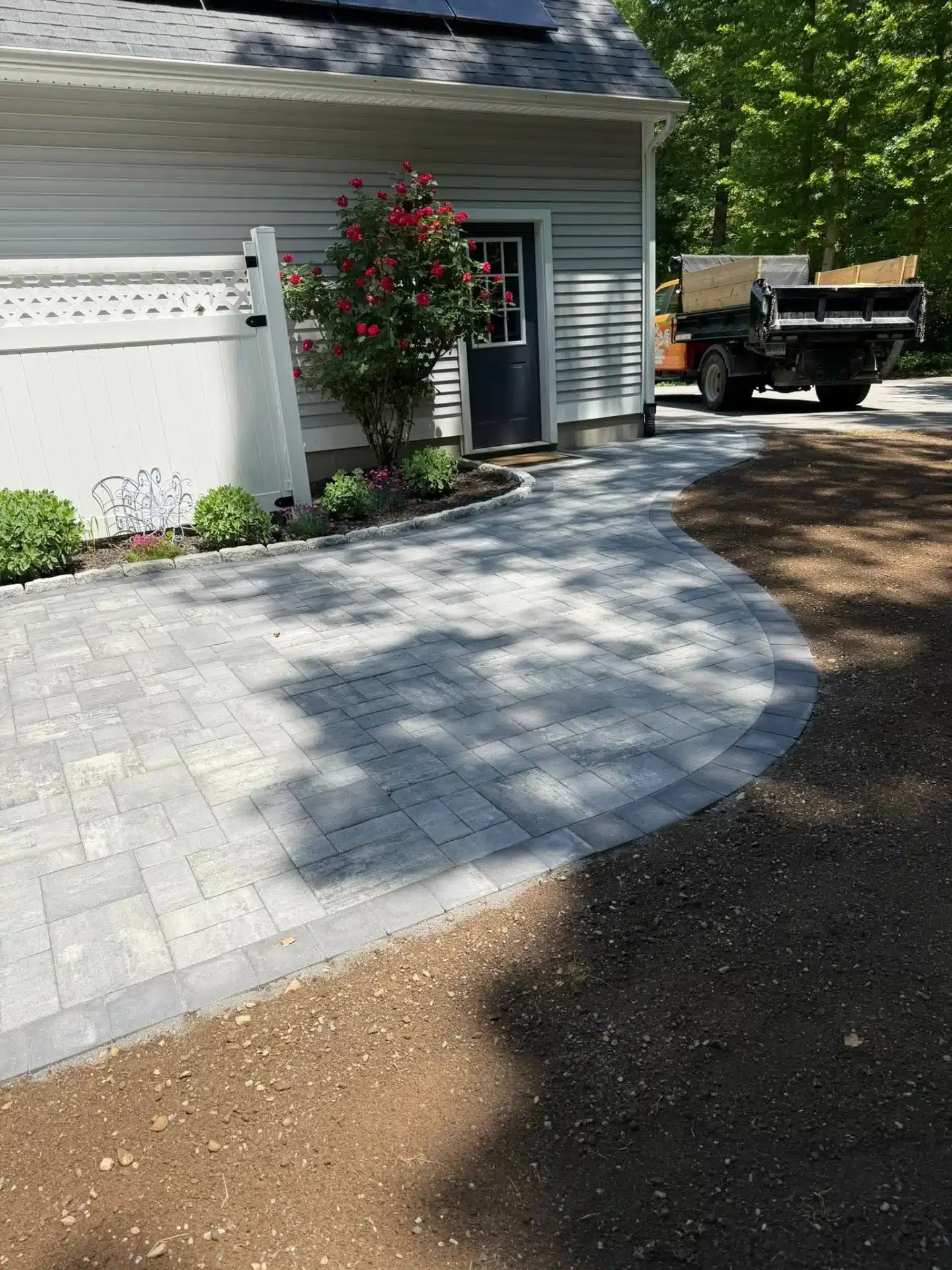 Custom paver patio hardscaping in Waterford, CT, featuring gray stone pavers, curved borders, and decorative garden edging.